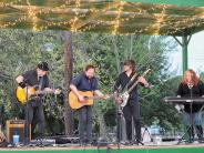 A bland plays on stage outside with three male guitarists and a female keyboard player.