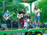 A band plays on stage outside with three male guitarists and one male drummer.