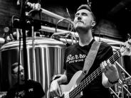 A man has his eyes closed while playing guitar inside at a brewery.