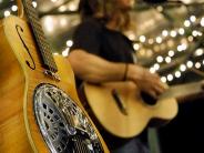 A picture of a guitar with an out of focus man in the background playing the guitar and singing.