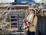 One male plays guitar wearing a khaki fedora and suit jacket.