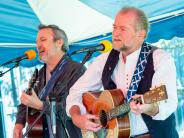 Two men play guitar and sing at a Scottish Festival outside.