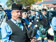 A man plays the bagpipes in a crowd with other bagpipe players.