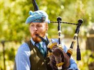 A man plays the bagpipes with trees behind him. 