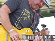 A man plays the guitar while looking down on stage outside. 